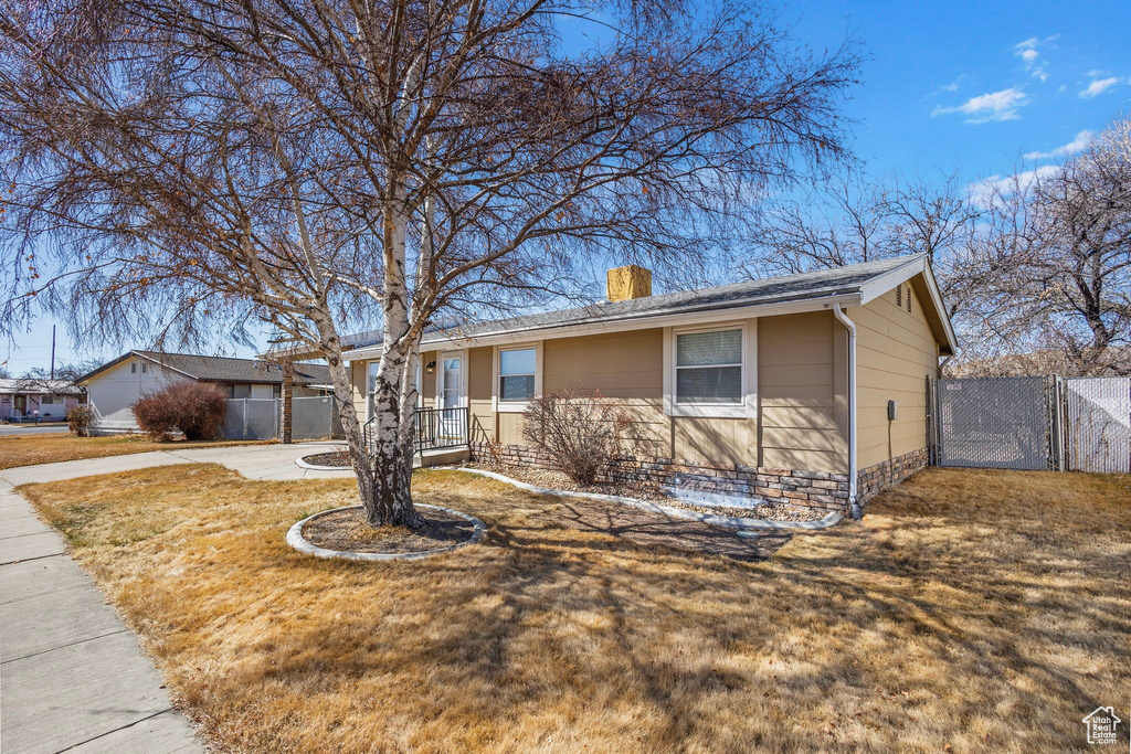 Ranch-style house featuring fence, concrete driveway, a front yard, a chimney, and a gate