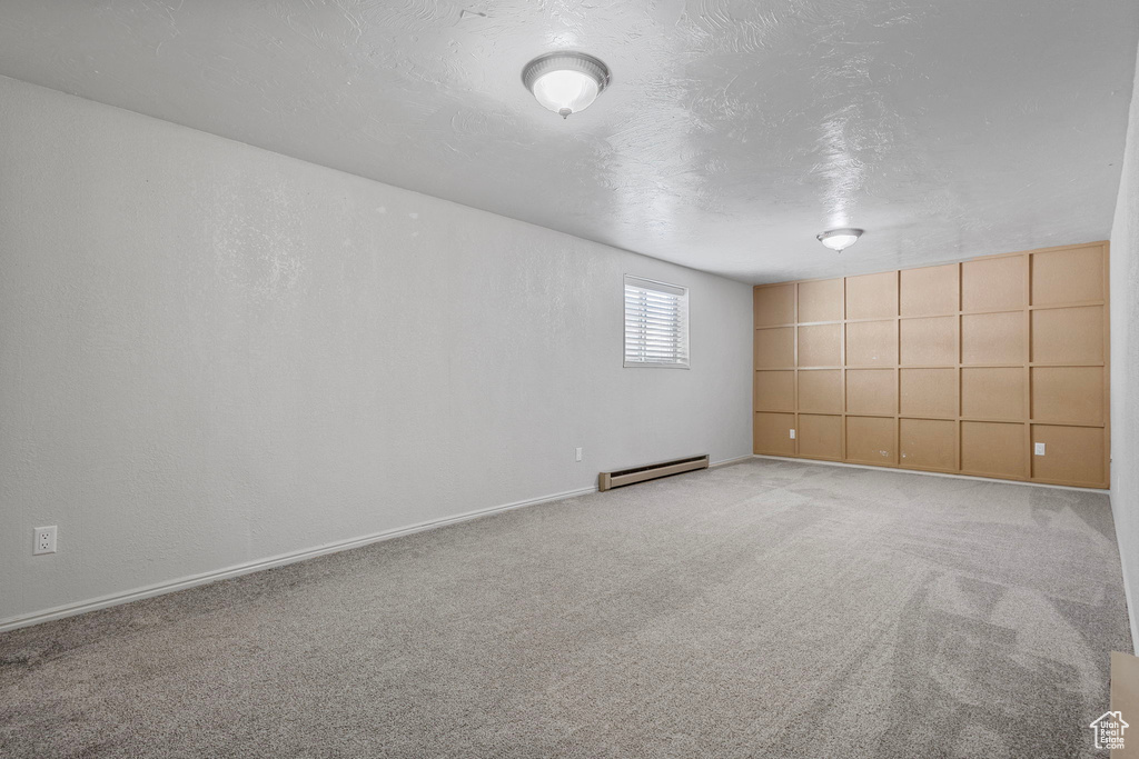 Carpeted empty room featuring a baseboard radiator, baseboards, a textured ceiling, and a textured wall