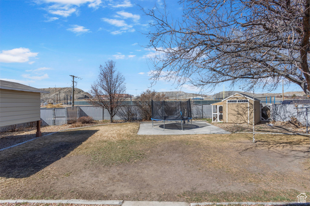 View of yard featuring a fenced backyard, a trampoline, an outdoor structure, and a shed