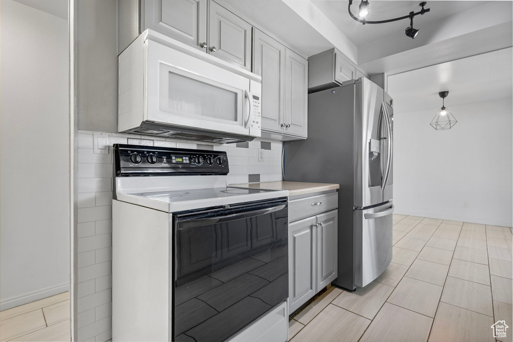 Kitchen featuring white microwave, gray cabinetry, light countertops, electric range oven, and stainless steel refrigerator with ice dispenser