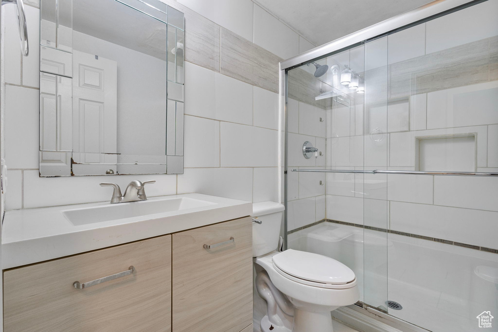 Full bathroom featuring vanity, tile walls, toilet, and a stall shower