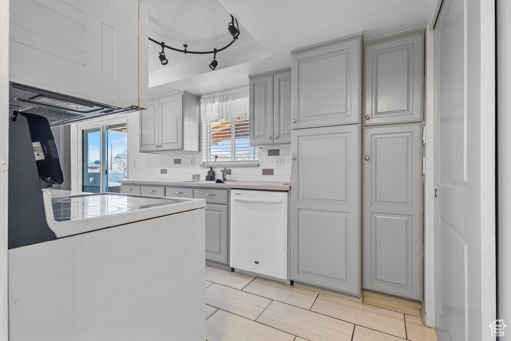 Kitchen featuring dishwasher, light countertops, decorative backsplash, gray cabinets, and a sink