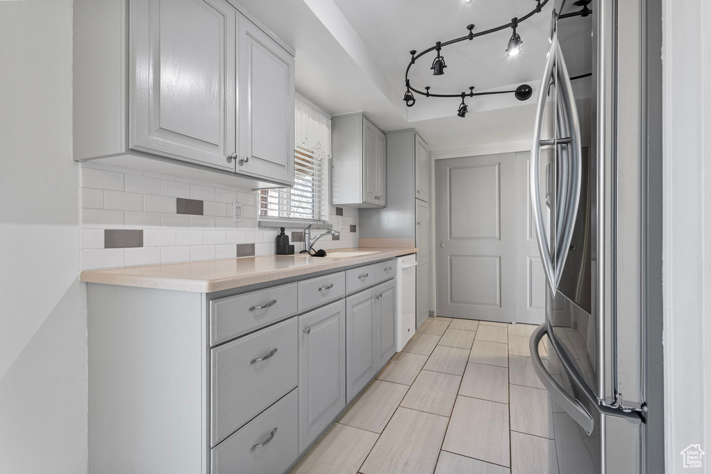 Kitchen with tasteful backsplash, light countertops, freestanding refrigerator, white dishwasher, and a sink