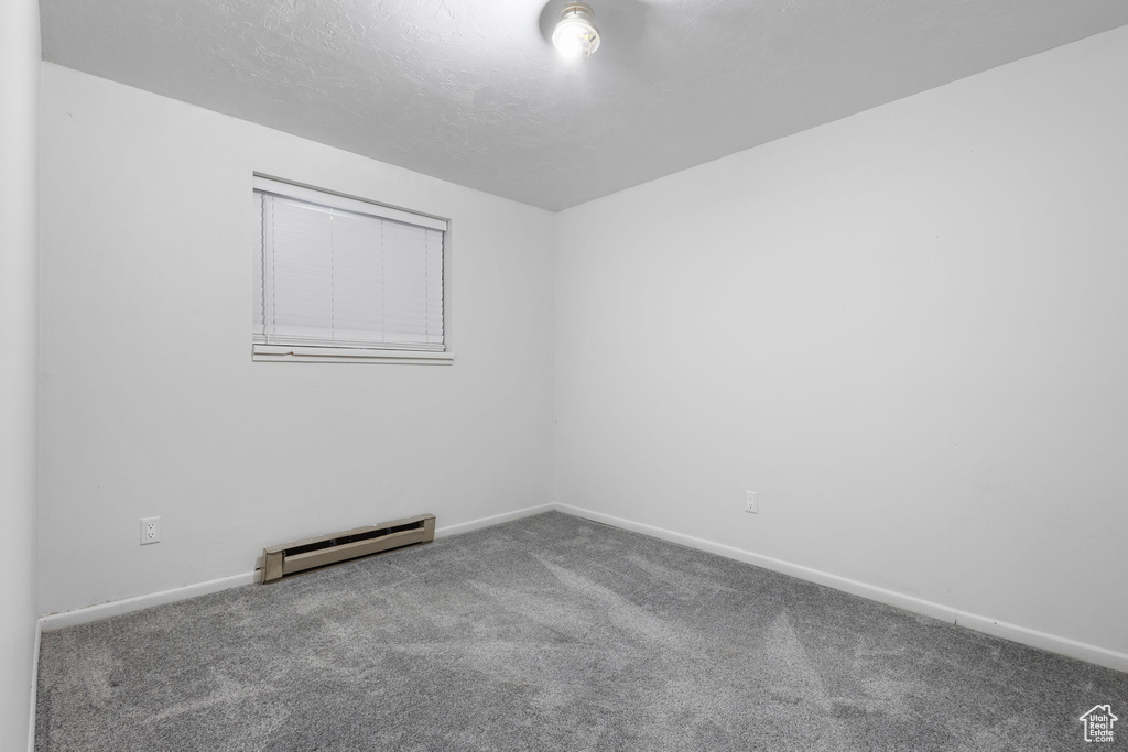 Empty room featuring a baseboard heating unit, baseboards, and carpet floors