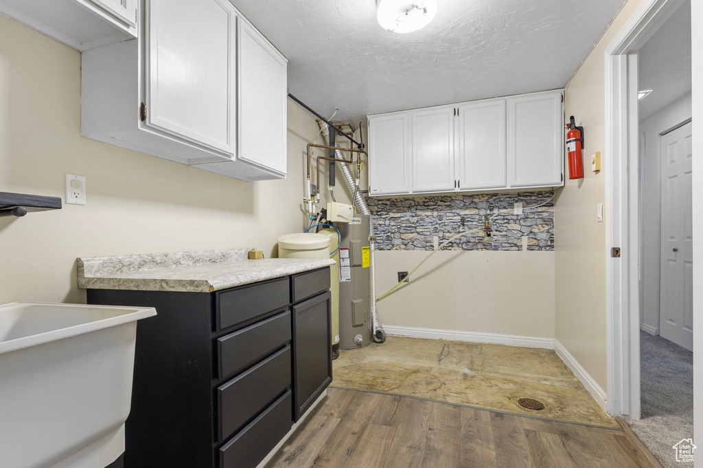 Clothes washing area with baseboards, light wood-style floors, laundry area, and electric water heater