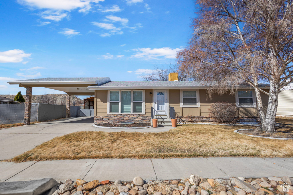 View of front facade with a front lawn, stone siding, fence, concrete driveway, and an attached carport