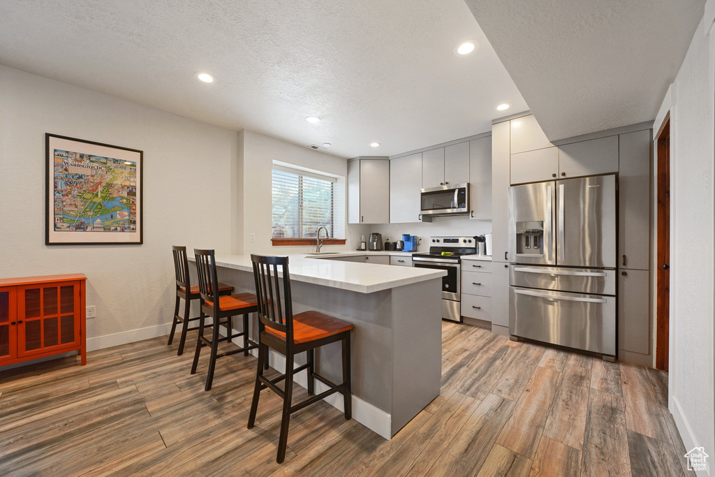 Kitchen with a breakfast bar, a peninsula, light wood finished floors, and appliances with stainless steel finishes