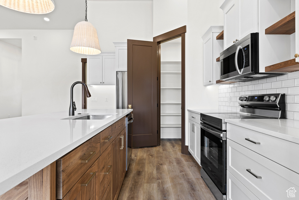 Kitchen featuring open shelves, a sink, backsplash, appliances with stainless steel finishes, and light countertops