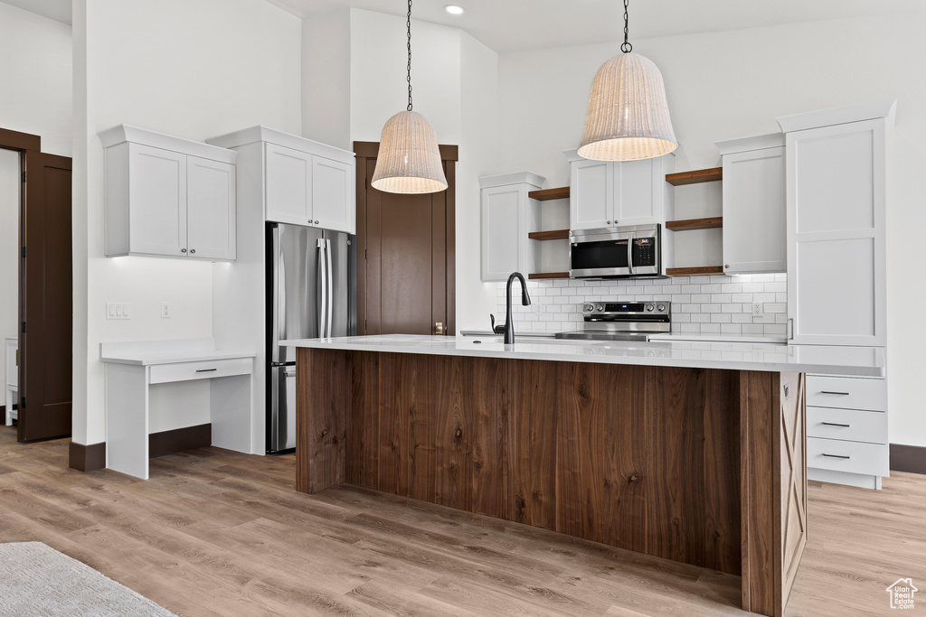 Kitchen featuring open shelves, a high ceiling, appliances with stainless steel finishes, and a sink