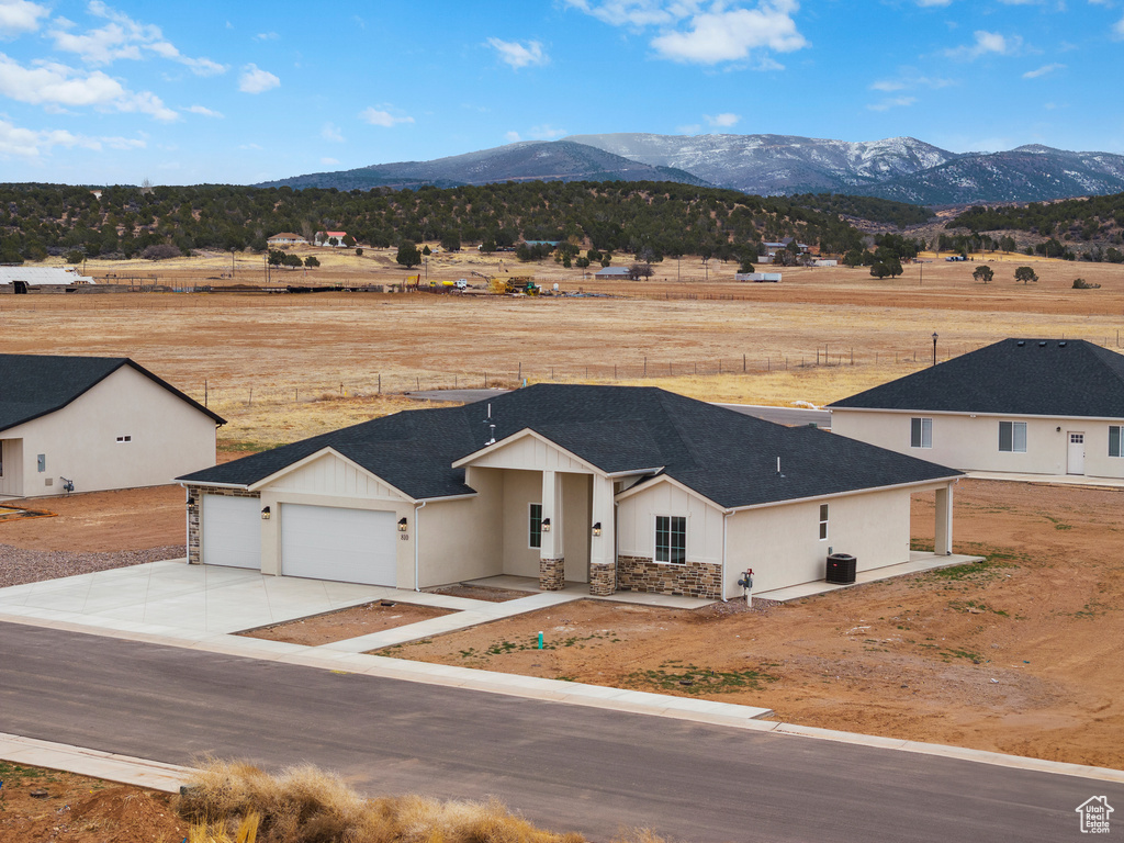 Exterior space with an attached garage, a shingled roof, concrete driveway, stone siding, and a mountain view