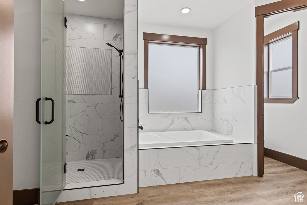 Full bath featuring baseboards, wood finished floors, a garden tub, and a stall shower