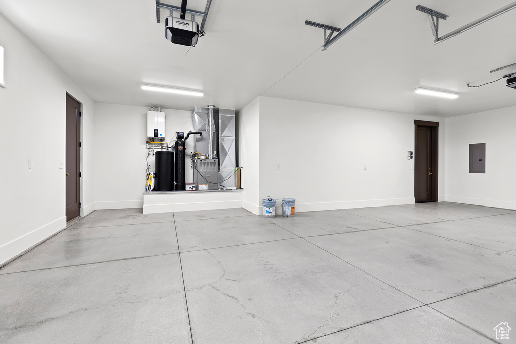 Garage featuring heating unit, electric panel, a garage door opener, and baseboards