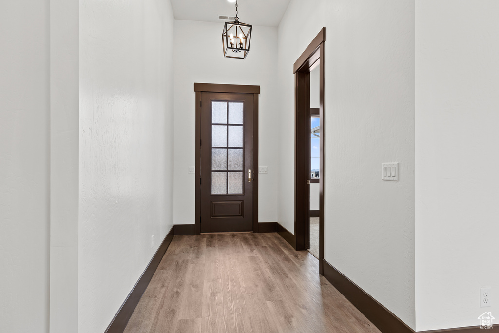 Doorway to outside with light wood finished floors, a notable chandelier, and baseboards