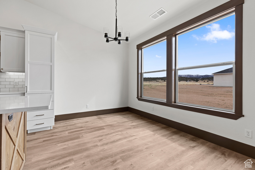 Unfurnished dining area featuring a notable chandelier, baseboards, visible vents, and light wood-type flooring