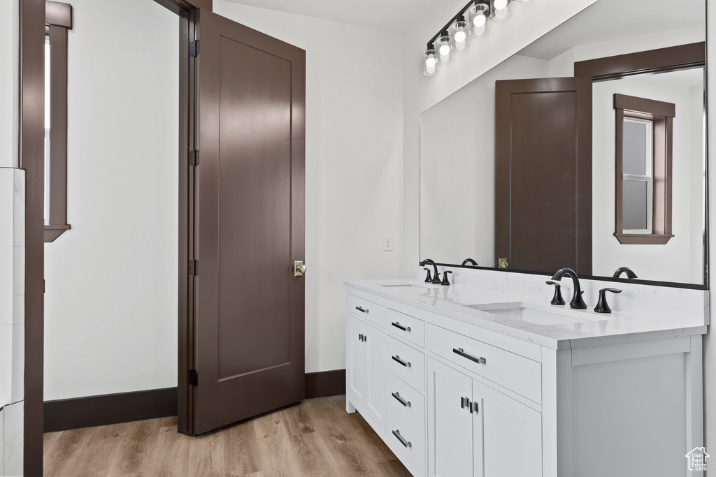 Bathroom featuring double vanity, wood finished floors, baseboards, and a sink