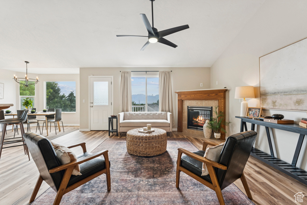 Living area with a tiled fireplace, a chandelier, wood finished floors, a ceiling fan, and lofted ceiling