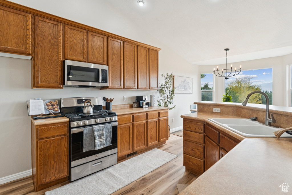 Kitchen featuring stainless steel appliances, vaulted ceiling, brown cabinetry, light wood-type flooring, and a chandelier