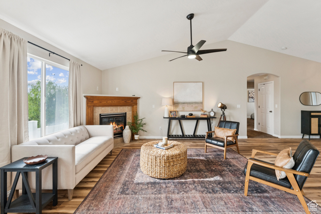 Living area featuring a ceiling fan, wood finished floors, arched walkways, a fireplace, and vaulted ceiling