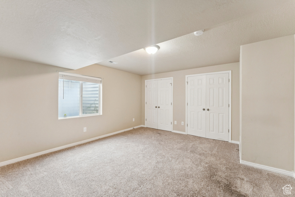 Unfurnished bedroom with multiple closets, carpet floors, and a textured ceiling