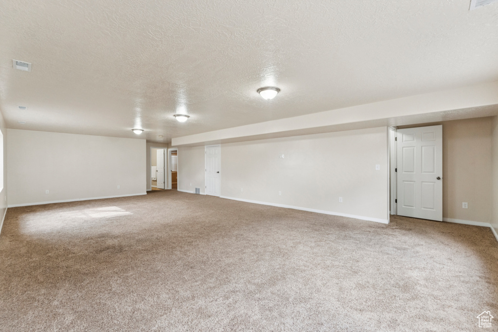 Carpeted empty room with a textured ceiling and baseboards