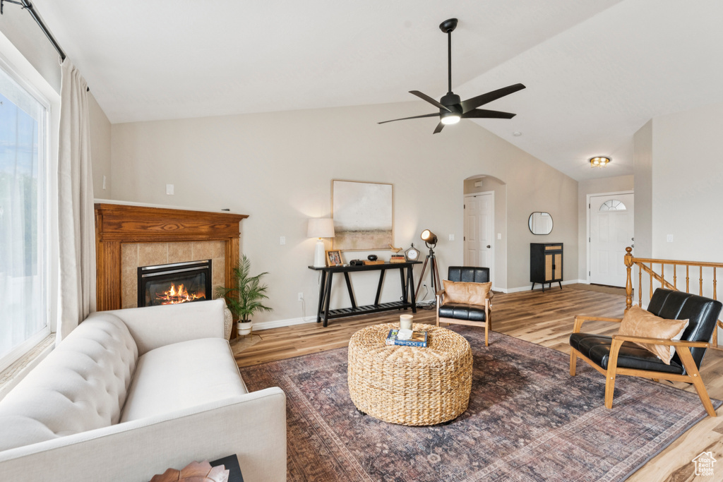 Living room featuring wood finished floors, healthy amount of natural light, lofted ceiling, a ceiling fan, and arched walkways