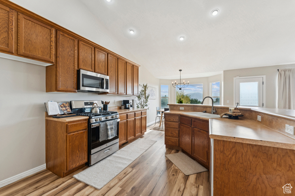 Kitchen with appliances with stainless steel finishes, brown cabinets, light wood finished floors, a chandelier, and recessed lighting