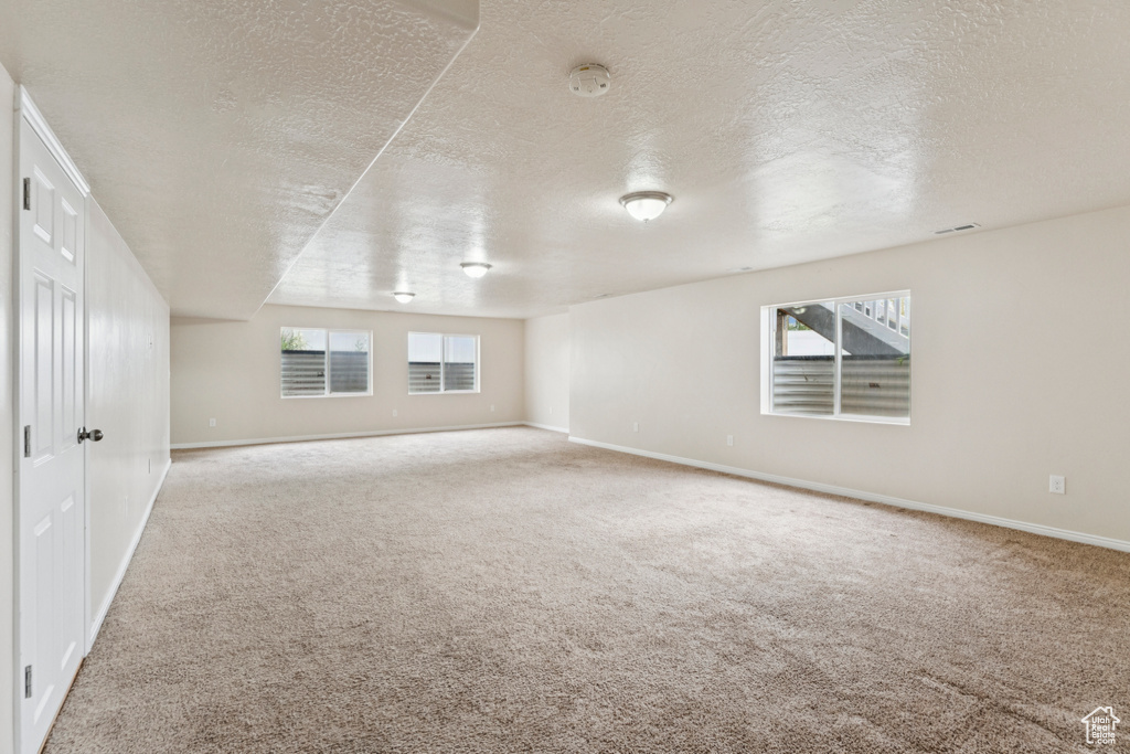 Carpeted empty room with a textured ceiling, healthy amount of natural light, and a smoke detector