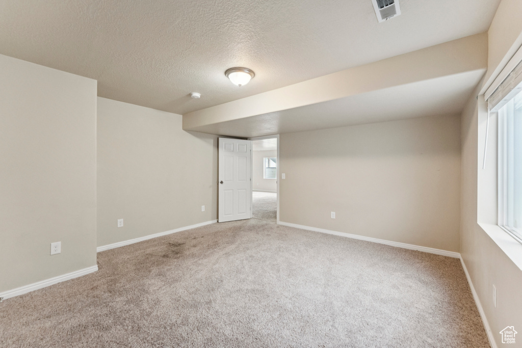 Carpeted empty room featuring a textured ceiling and a smoke detector