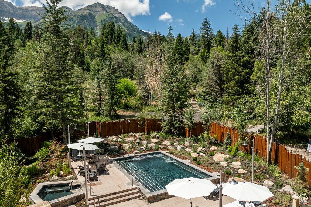 View of swimming pool featuring a fenced backyard, a mountain view, a wooded view, and a jacuzzi