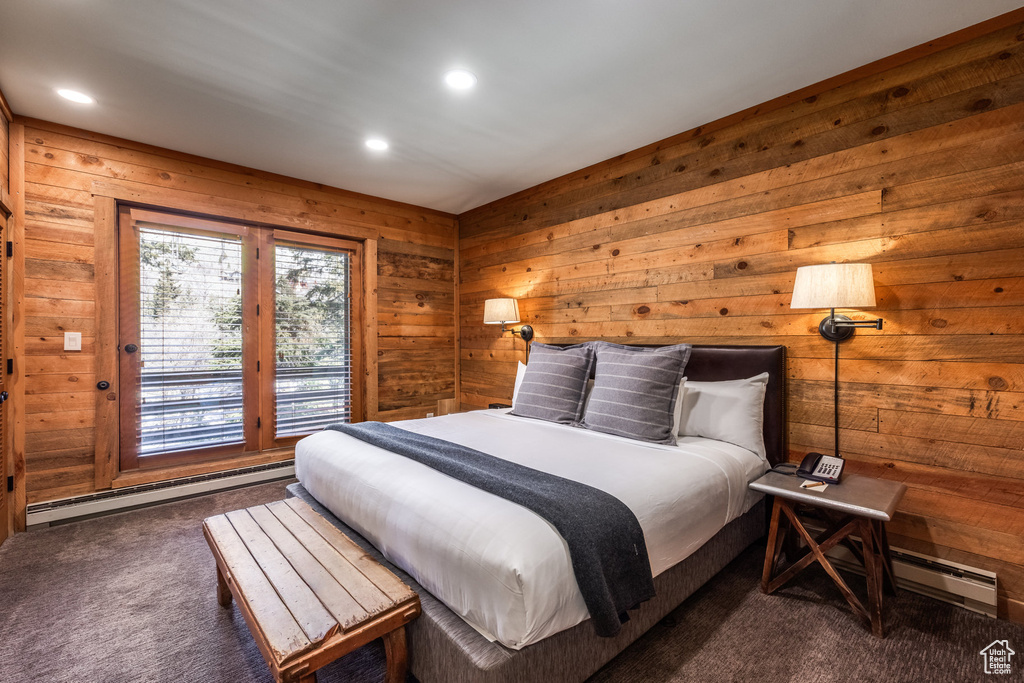 Bedroom featuring dark colored carpet, access to exterior, wooden walls, a baseboard heating unit, and recessed lighting