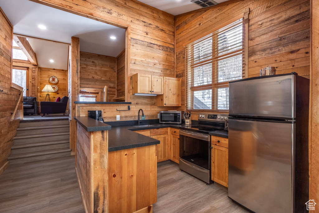 Kitchen with stainless steel appliances, a peninsula, dark countertops, wood walls, and light wood-type flooring