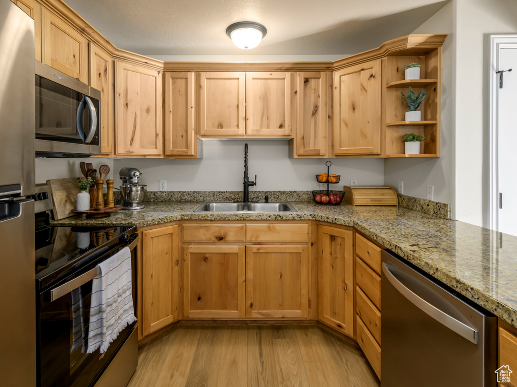 Kitchen featuring a sink, light brown cabinetry, light wood-style floors, stainless steel appliances, and open shelves