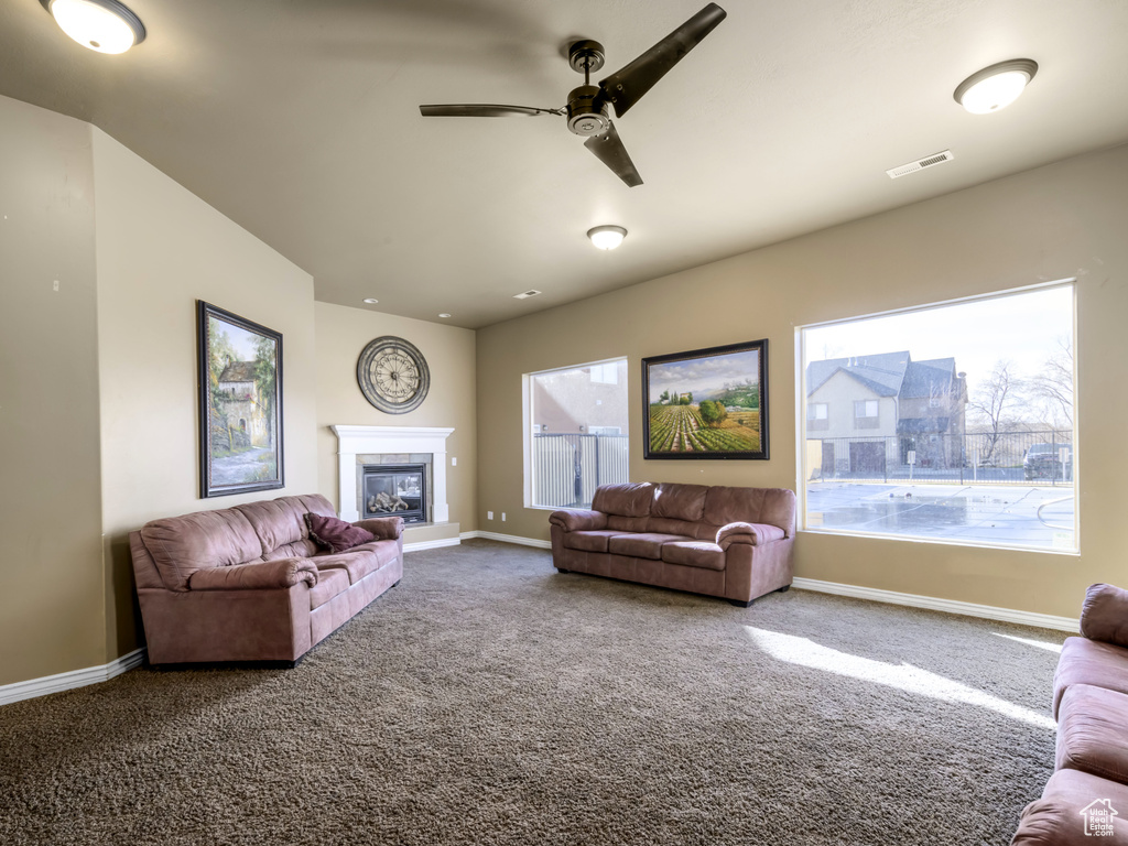 Living room with carpet, visible vents, baseboards, ceiling fan, and a glass covered fireplace