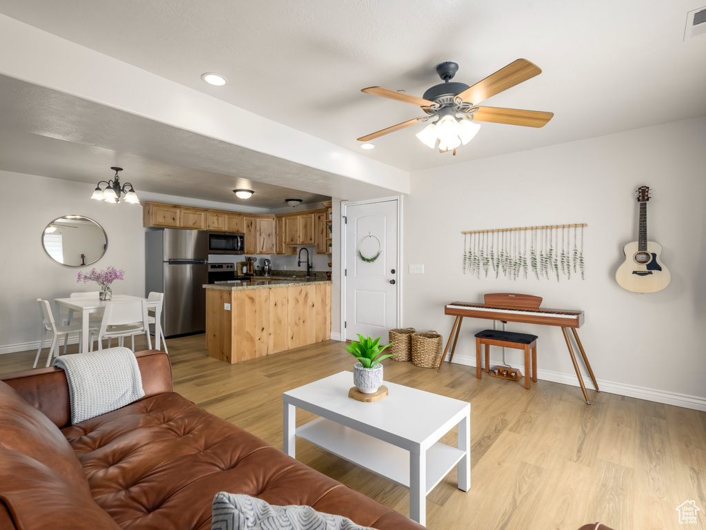 Living area featuring visible vents, ceiling fan with notable chandelier, light wood-type flooring, and baseboards