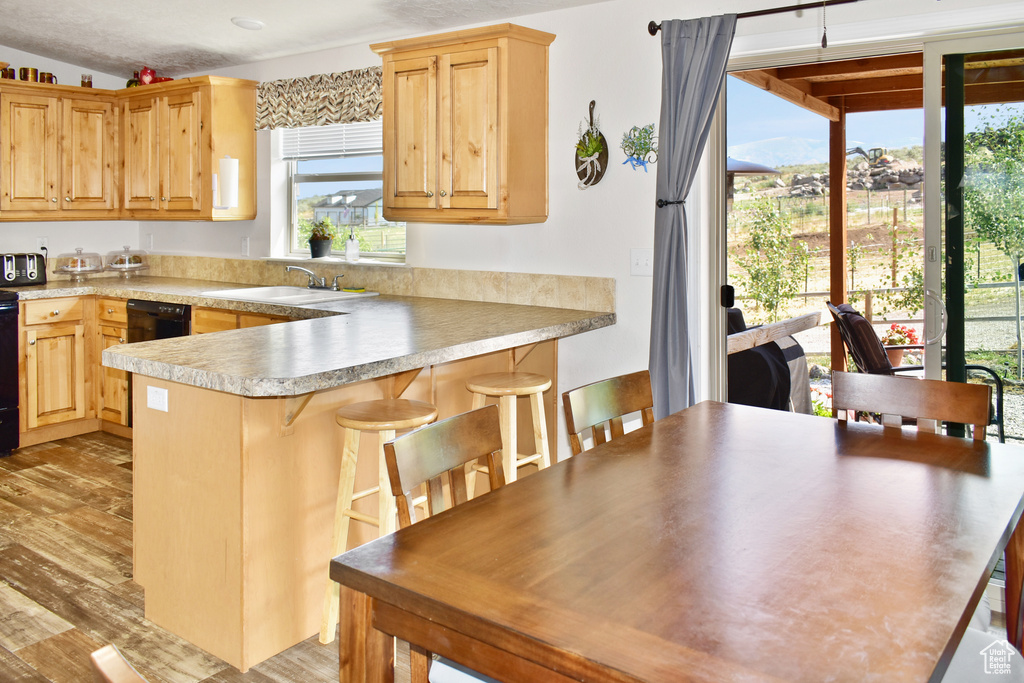 Kitchen with light brown cabinets, light wood-type flooring, a peninsula, a kitchen breakfast bar, and a sink