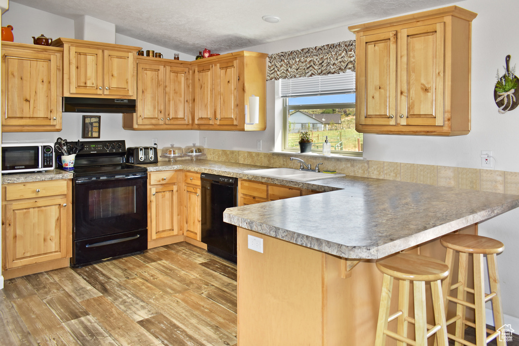 Kitchen with a peninsula, a sink, black appliances, light wood-style floors, and under cabinet range hood