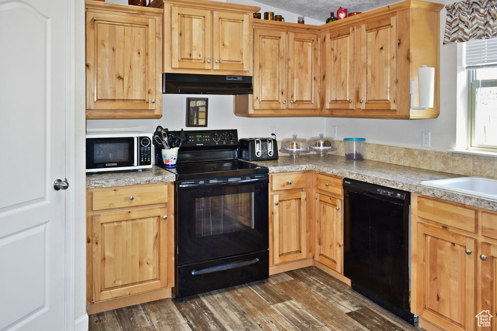 Kitchen featuring dark wood-type flooring, black appliances, under cabinet range hood, a sink, and light countertops