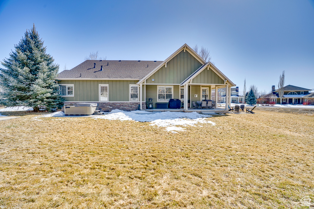 Back of house with a yard, a hot tub, stone siding, a patio area, and board and batten siding