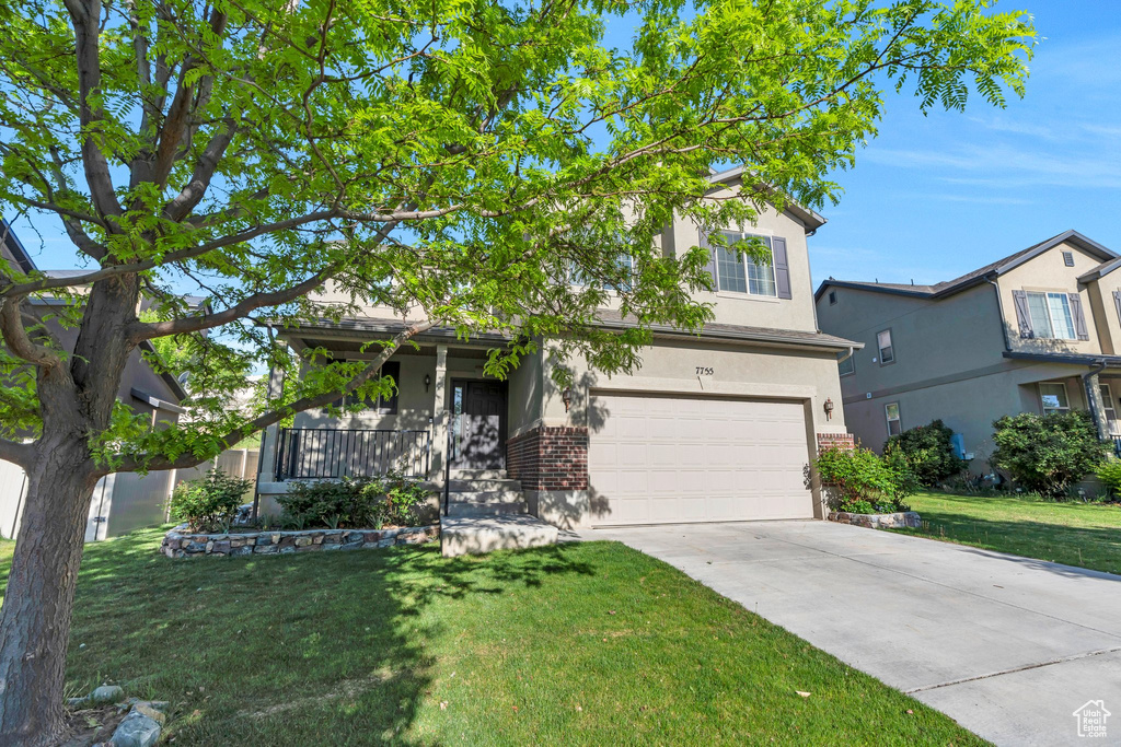 View of property hidden behind natural elements with stucco siding, a garage, driveway, and a front lawn