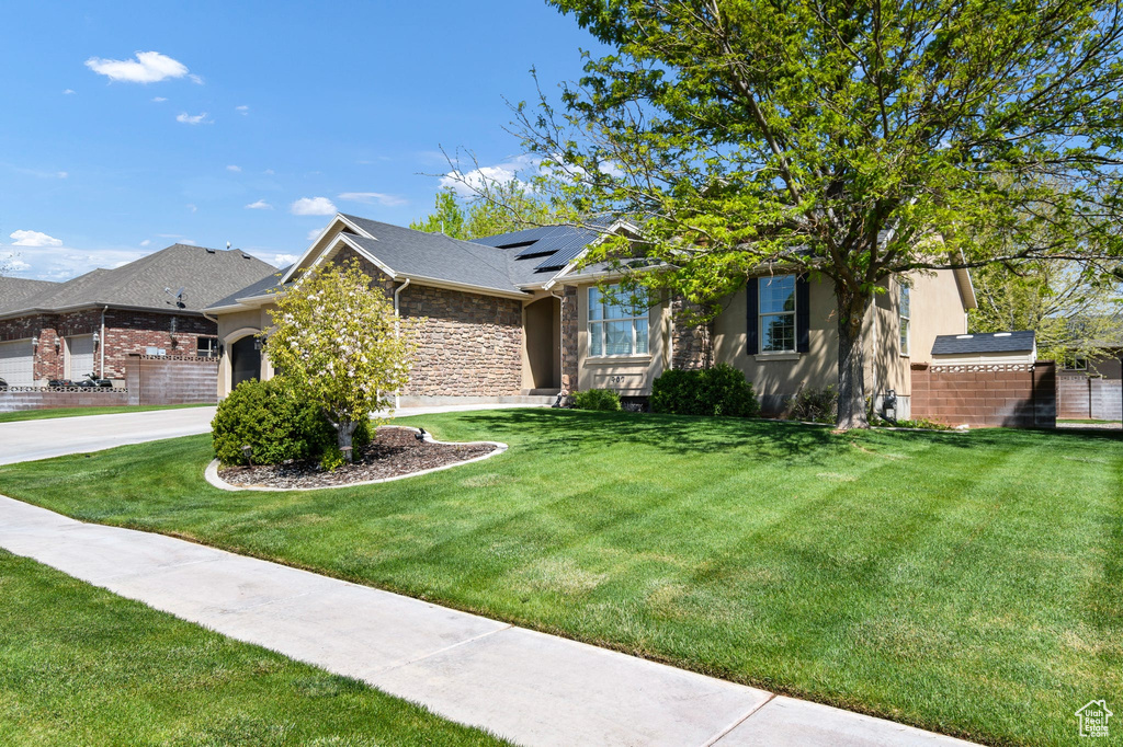 View of front of home featuring roof mounted solar panels, stone siding, a front yard, and a garage