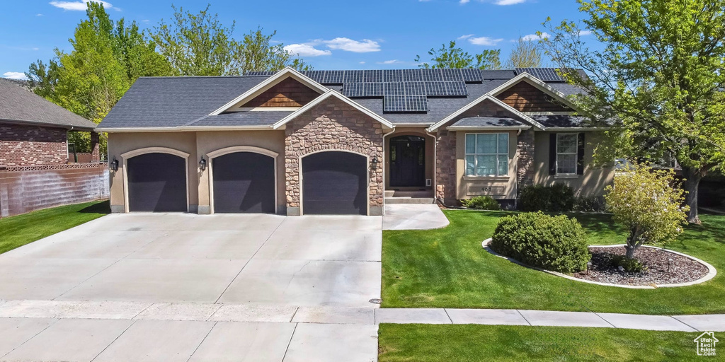 View of front of house with stone siding, an attached garage, a front yard, driveway, and solar panels