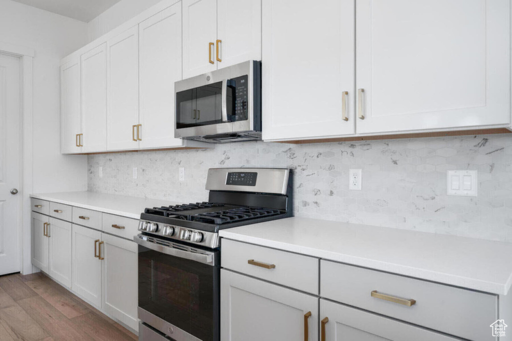 Kitchen with stainless steel appliances, tasteful backsplash, wood finished floors, and light countertops