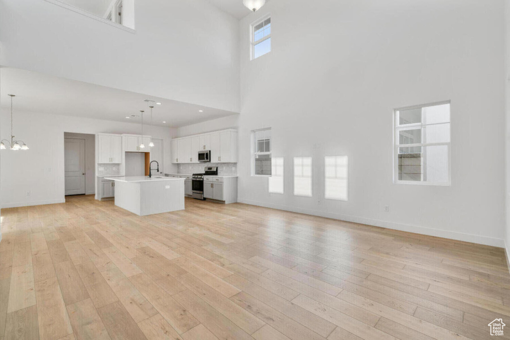 Unfurnished living room featuring a sink, baseboards, a notable chandelier, and light wood finished floors