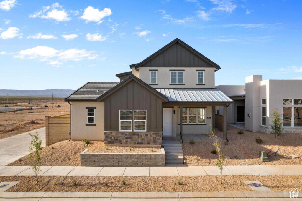 View of front of house with a porch, board and batten siding, stone siding, and metal roof