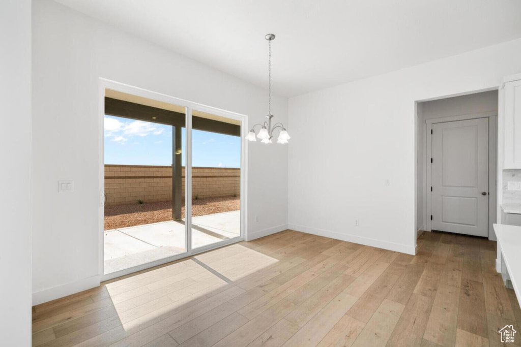 Spare room with a notable chandelier, baseboards, and light wood-style floors