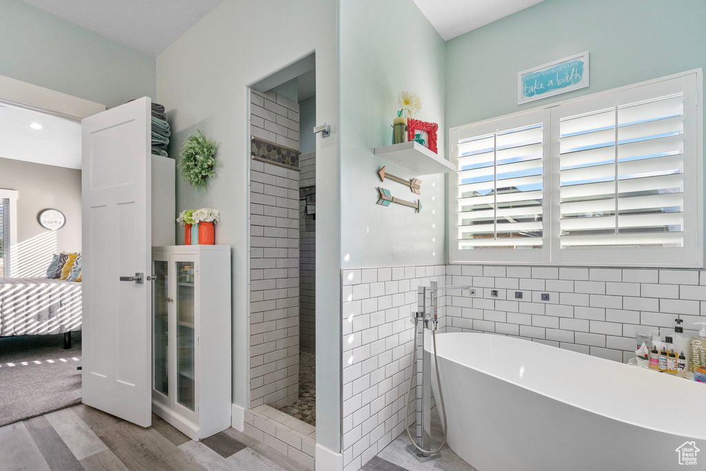 Bathroom with tile walls, a freestanding tub, wood finished floors, and walk in shower