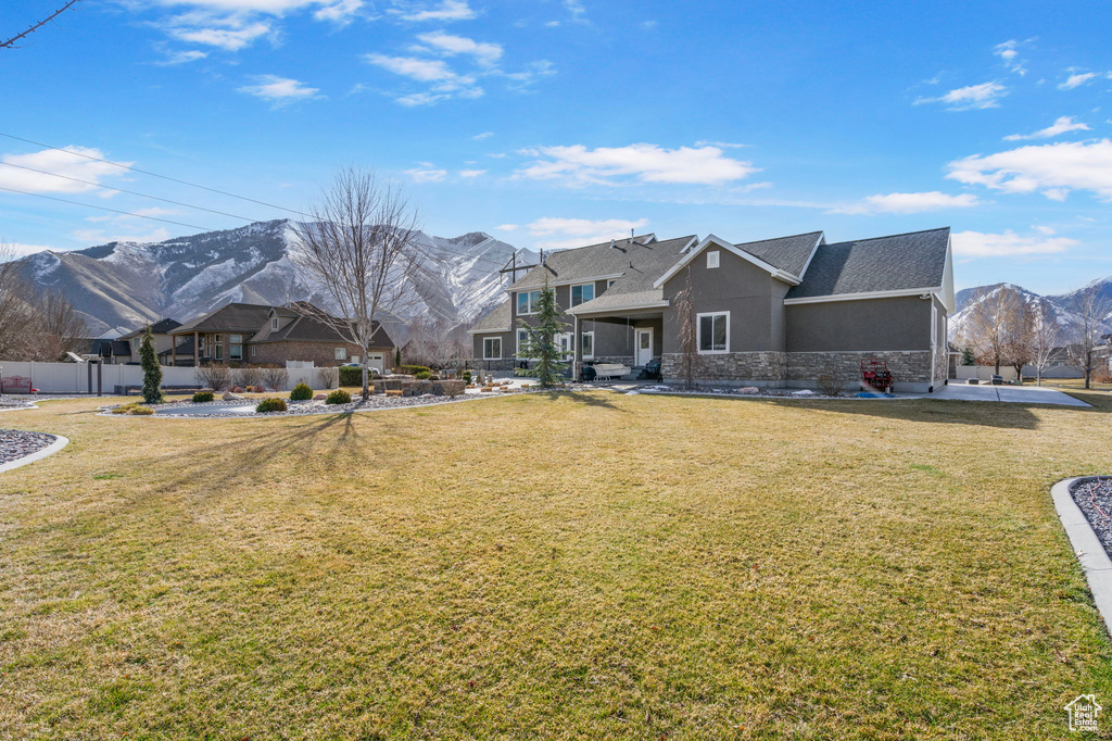 Rear view of house featuring stucco siding, a lawn, a mountain view, and fence