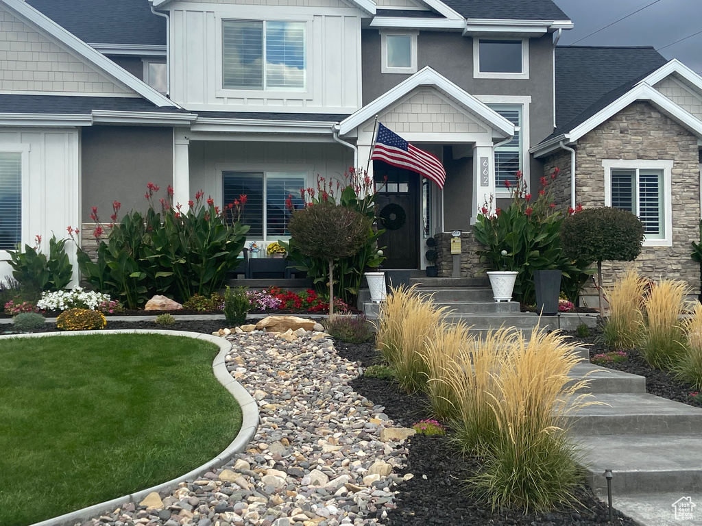 View of front of home with board and batten siding, a shingled roof, stone siding, and a front lawn