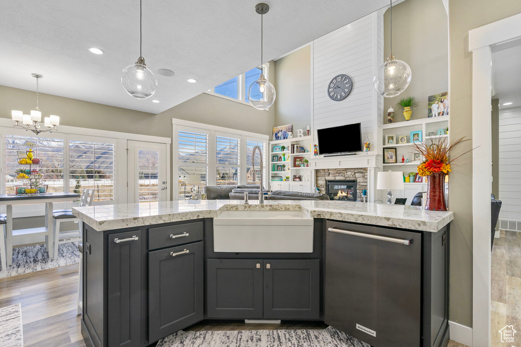 Kitchen featuring light wood finished floors, open floor plan, dishwasher, a stone fireplace, and a sink