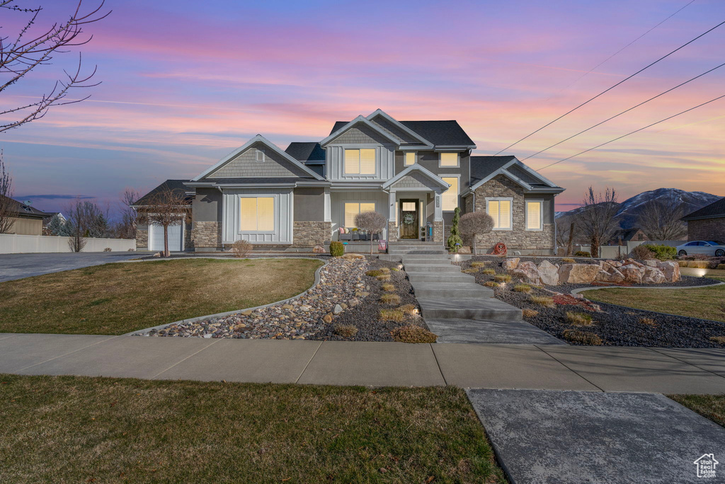 Craftsman-style home featuring a front lawn, stone siding, a garage, and driveway